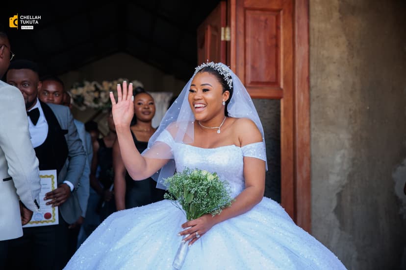 Bride waving from church entrance in white wedding gown with veil
