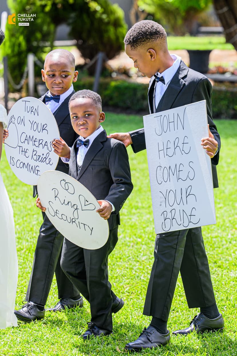Three young ring bearers in black suits holding wedding ceremony signs
