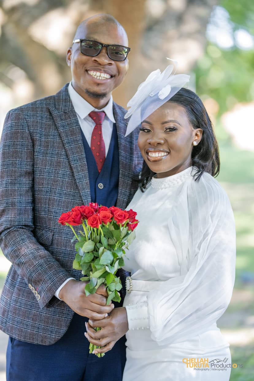 Happy couple portrait - groom in checkered suit, bride with fascinator and red roses