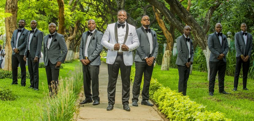 Formal groomsmen lineup - groom in white jacket center with 8+ groomsmen in gray suits