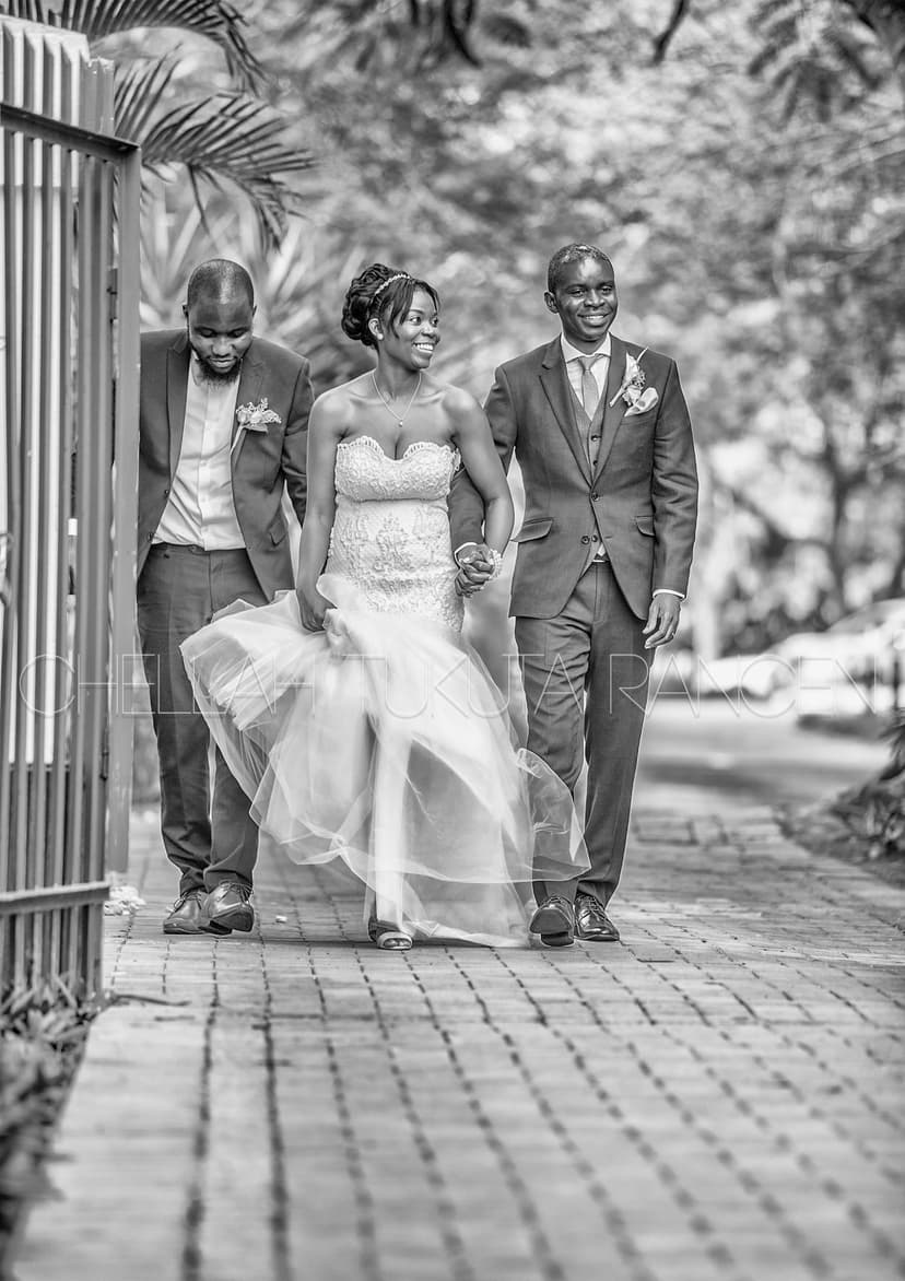 Black and white artistic shot of bride in beaded gown walking with groom and father on brick pathway